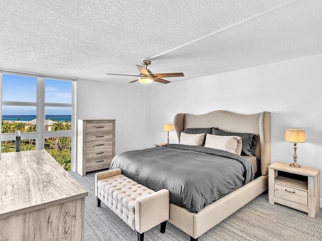 carpeted bedroom with a water view, a textured ceiling, and ceiling fan