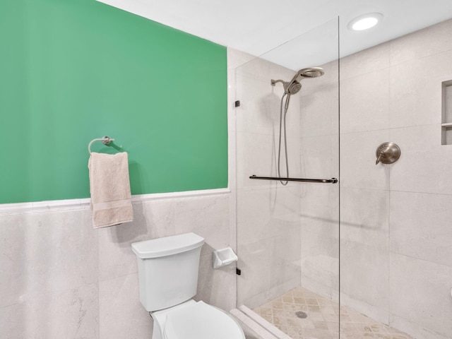 bathroom featuring toilet, tiled shower, and tile walls