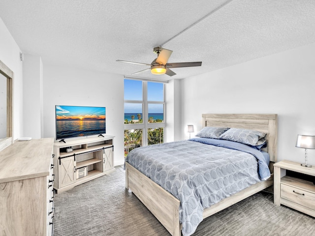 bedroom with a textured ceiling, dark colored carpet, expansive windows, and ceiling fan