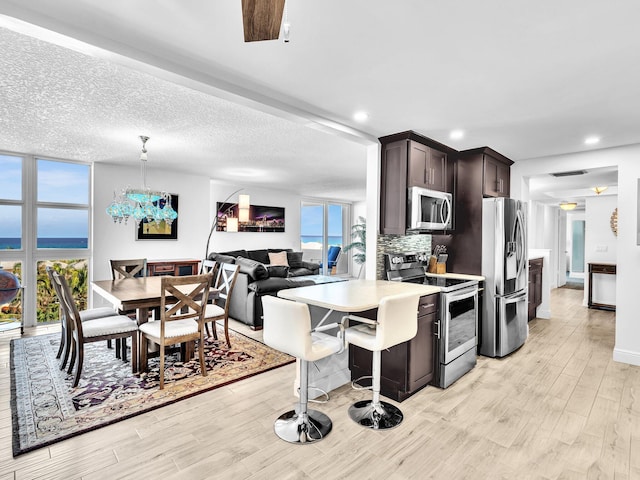 kitchen with stainless steel appliances, dark brown cabinetry, hanging light fixtures, a kitchen breakfast bar, and light wood-type flooring