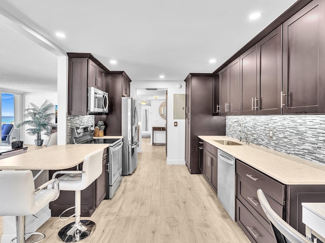 kitchen featuring stainless steel appliances, light hardwood / wood-style floors, sink, a breakfast bar, and decorative backsplash