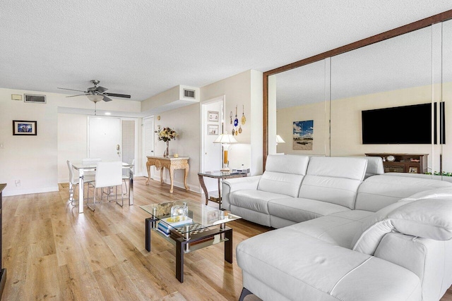 living room featuring ceiling fan, light hardwood / wood-style flooring, and a textured ceiling