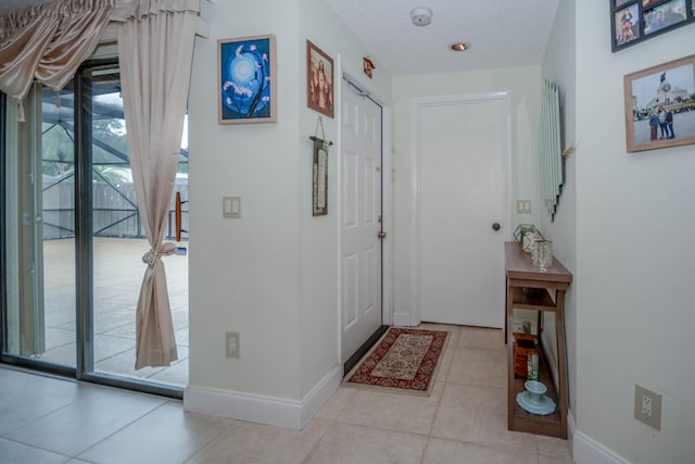 doorway to outside with a textured ceiling, baseboards, and light tile patterned floors