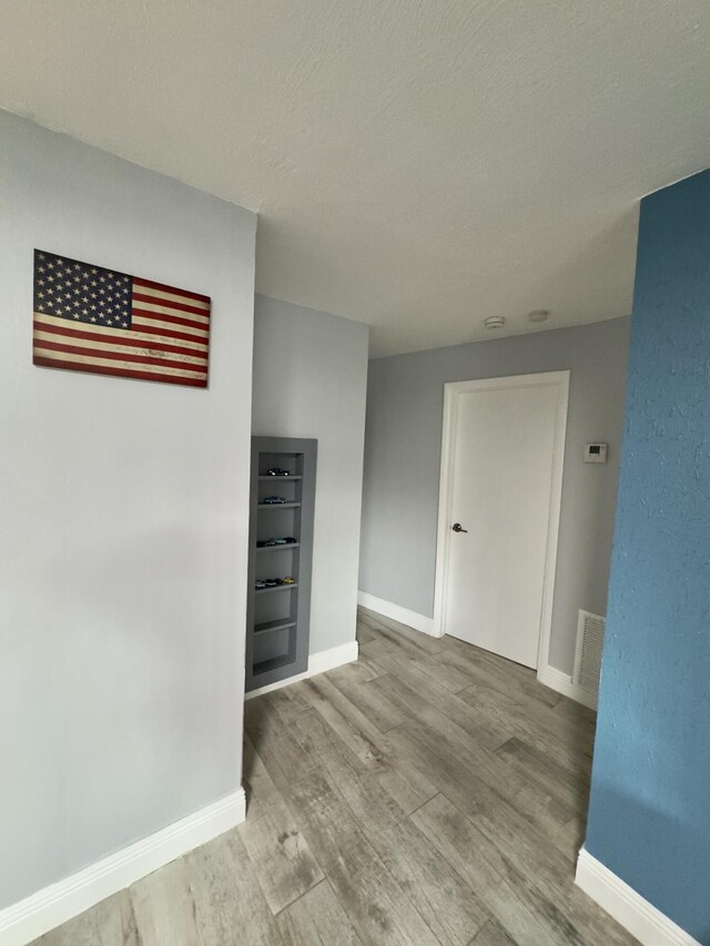 unfurnished room with visible vents, a textured ceiling, baseboards, and wood finished floors