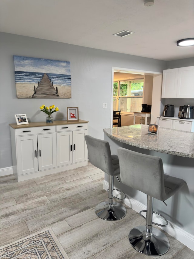 kitchen with light stone counters, white cabinetry, a kitchen bar, and light hardwood / wood-style floors