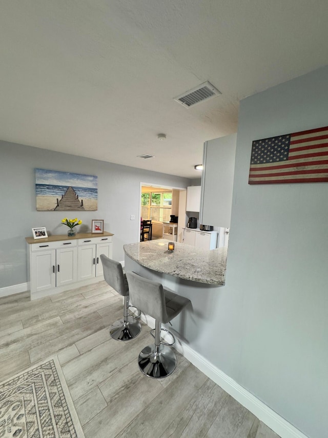 kitchen with white cabinetry, light stone counters, light wood-type flooring, and kitchen peninsula