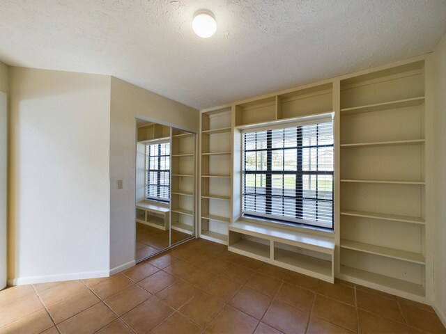 tiled empty room with a wealth of natural light, a textured ceiling, and built in features