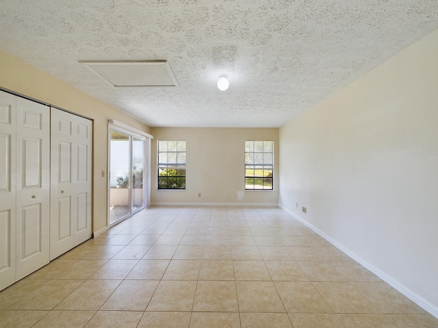 unfurnished bedroom with light tile patterned floors, attic access, a textured ceiling, access to outside, and baseboards