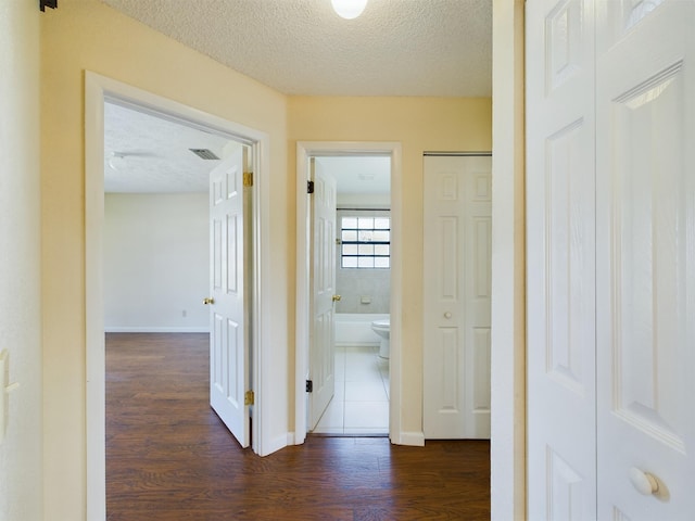 hallway featuring baseboards, a textured ceiling, visible vents, and dark wood-style flooring