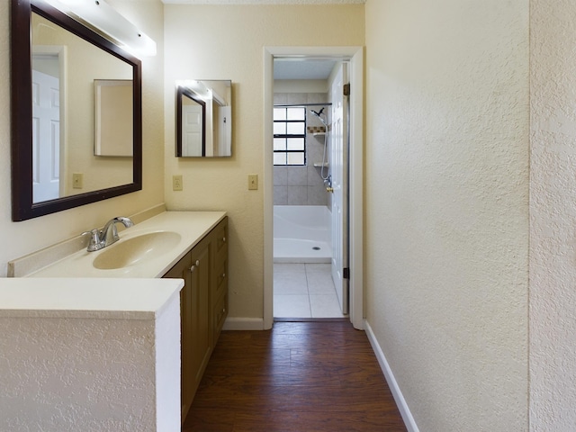 bathroom featuring baseboards, a textured wall, wood finished floors, walk in shower, and vanity