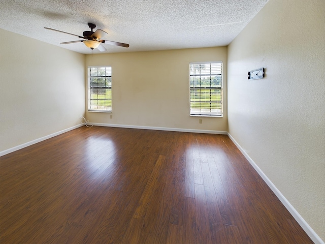 empty room with a textured ceiling, ceiling fan, plenty of natural light, and dark hardwood / wood-style flooring