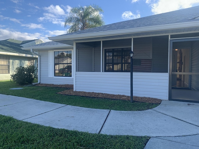 view of side of property with a sunroom, roof with shingles, and a yard