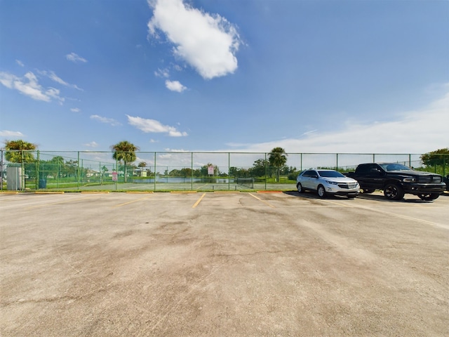 uncovered parking lot featuring a tennis court and fence