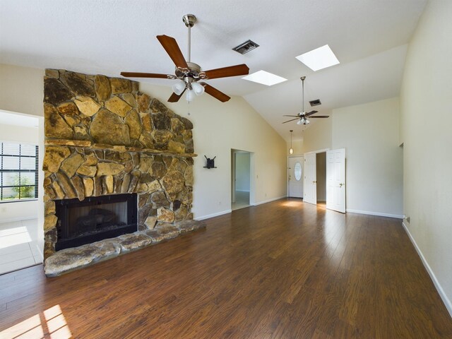 unfurnished living room with ceiling fan, dark hardwood / wood-style flooring, high vaulted ceiling, a skylight, and a stone fireplace