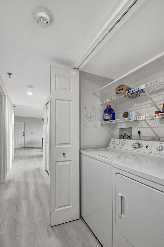 clothes washing area featuring light wood-type flooring and washer and clothes dryer