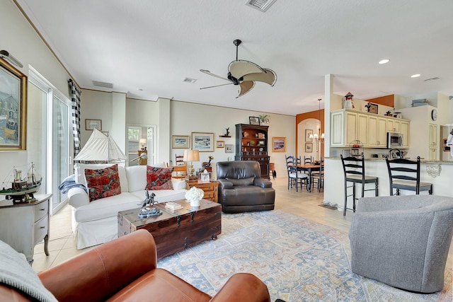 tiled living room with ceiling fan with notable chandelier