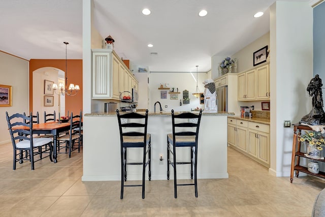 kitchen featuring cream cabinets, decorative light fixtures, and light stone counters