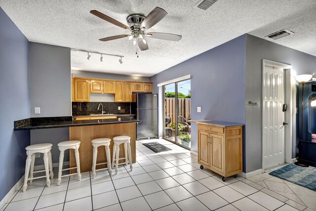 kitchen featuring light brown cabinetry, ceiling fan, light tile patterned flooring, and a textured ceiling