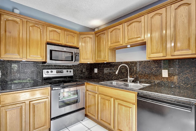 kitchen with stainless steel appliances, sink, a textured ceiling, light tile patterned flooring, and dark stone countertops