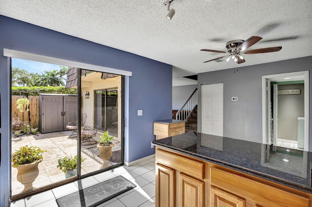 kitchen featuring ceiling fan, light tile patterned floors, a textured ceiling, and dark stone countertops