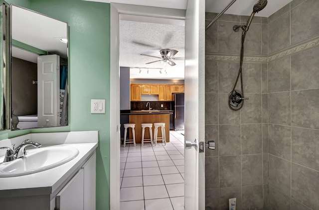 bathroom with ceiling fan, tile patterned flooring, backsplash, a tile shower, and vanity