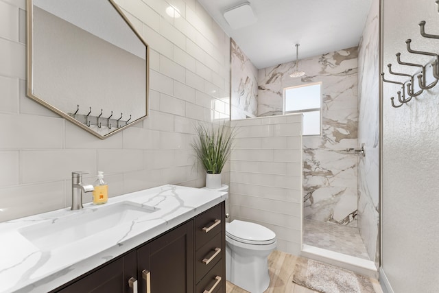 bathroom featuring a tile shower, toilet, vanity, tile walls, and hardwood / wood-style flooring