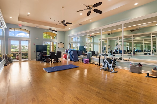 gym featuring french doors, a towering ceiling, light wood-type flooring, a raised ceiling, and ceiling fan