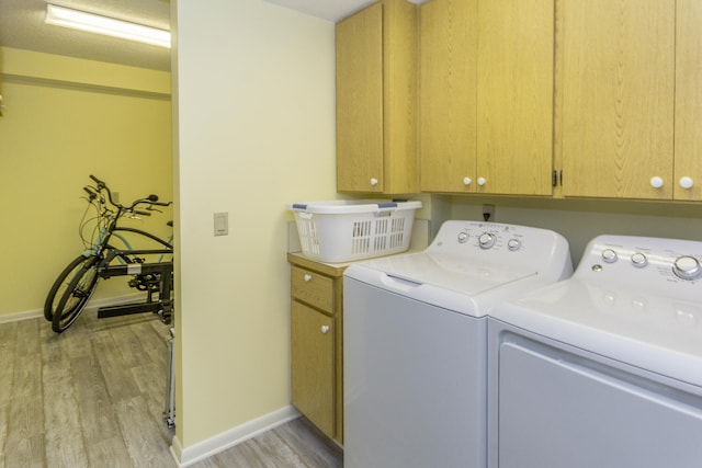 clothes washing area with cabinets, light wood-type flooring, and washing machine and dryer