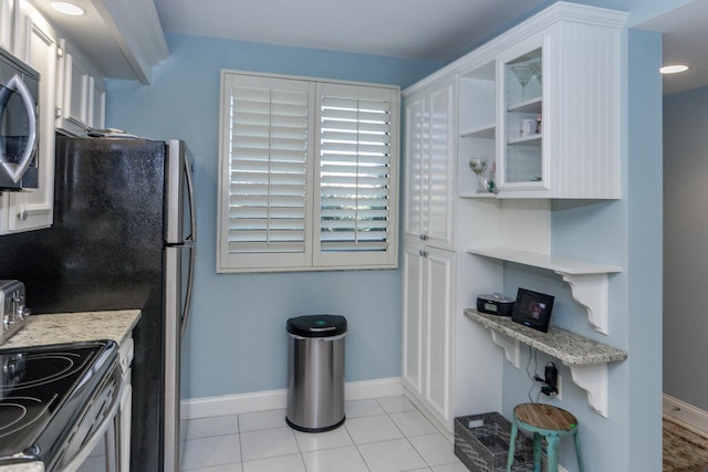 kitchen with electric range, light stone countertops, white cabinetry, and light tile patterned floors