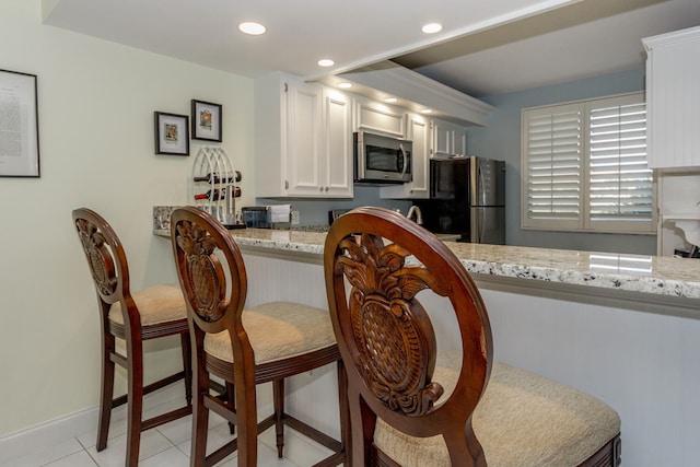 kitchen featuring white cabinets, a breakfast bar area, light tile patterned flooring, light stone counters, and stainless steel appliances