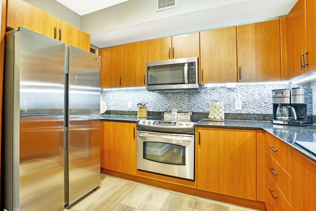 kitchen featuring appliances with stainless steel finishes, light hardwood / wood-style flooring, dark stone countertops, and tasteful backsplash