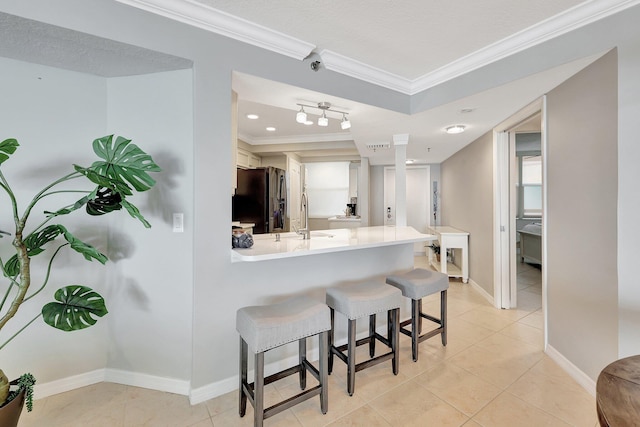 kitchen with black fridge, crown molding, white cabinetry, kitchen peninsula, and a breakfast bar area