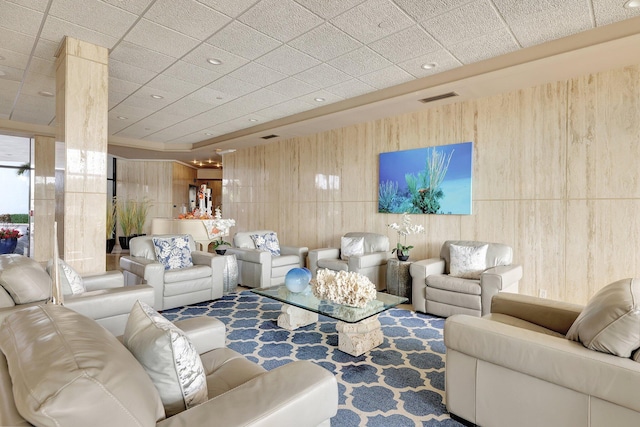 living room featuring a paneled ceiling and wooden walls