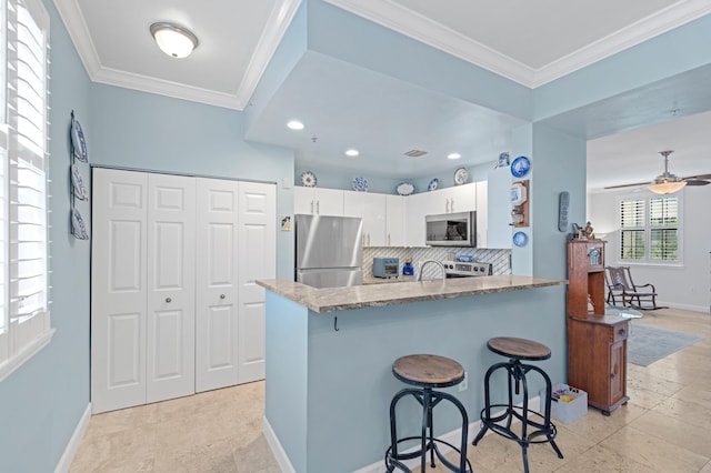 kitchen featuring kitchen peninsula, tasteful backsplash, white cabinetry, appliances with stainless steel finishes, and a breakfast bar area