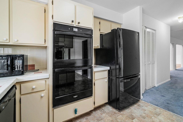 kitchen featuring black appliances, cream cabinetry, backsplash, and light colored carpet