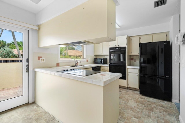 kitchen with tasteful backsplash, tile countertops, black appliances, cream cabinetry, and sink