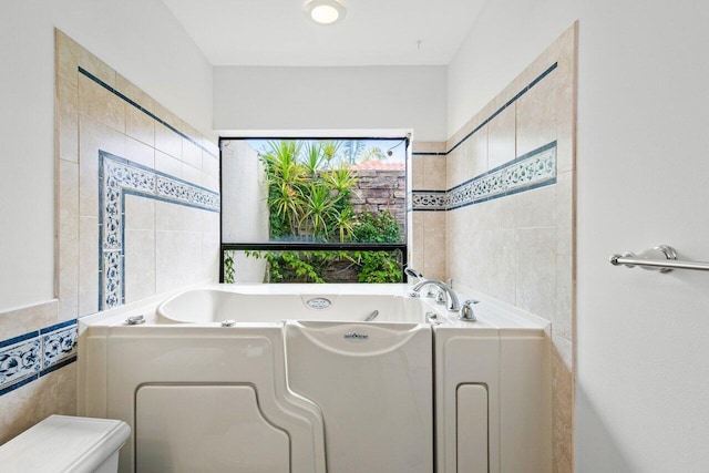 bathroom with a bathtub, toilet, and tile walls