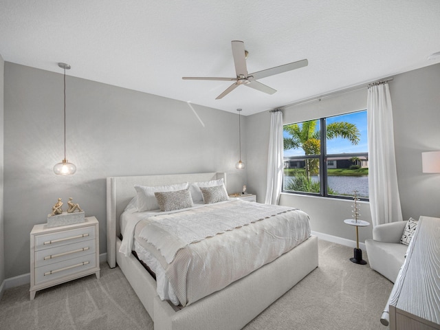 bedroom with light carpet, a water view, and ceiling fan