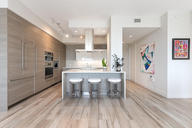 kitchen featuring island exhaust hood, light hardwood / wood-style flooring, a kitchen bar, and tasteful backsplash