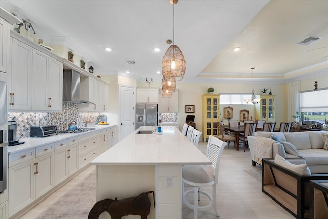 kitchen with a center island with sink, a breakfast bar, white cabinetry, wall chimney exhaust hood, and decorative light fixtures