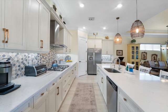 kitchen featuring white cabinets, appliances with stainless steel finishes, sink, wall chimney exhaust hood, and decorative light fixtures