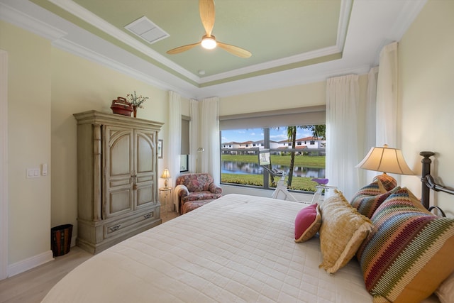 bedroom with light wood-type flooring, a raised ceiling, ceiling fan, a water view, and crown molding