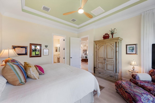 bedroom featuring a tray ceiling, ensuite bath, ornamental molding, light hardwood / wood-style floors, and ceiling fan