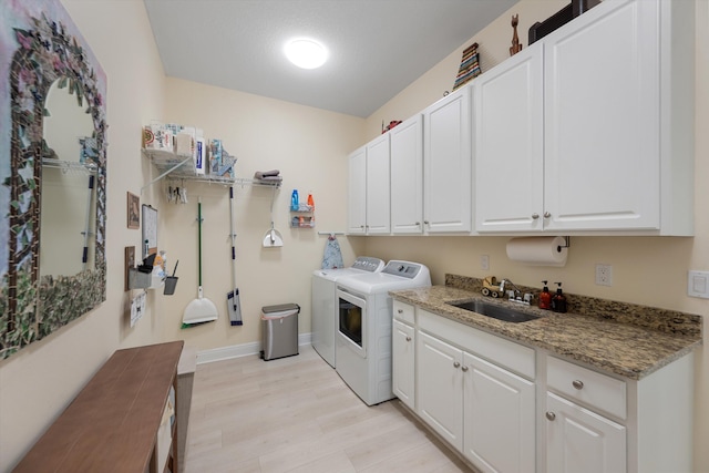 clothes washing area featuring cabinets, sink, washing machine and clothes dryer, and light wood-type flooring