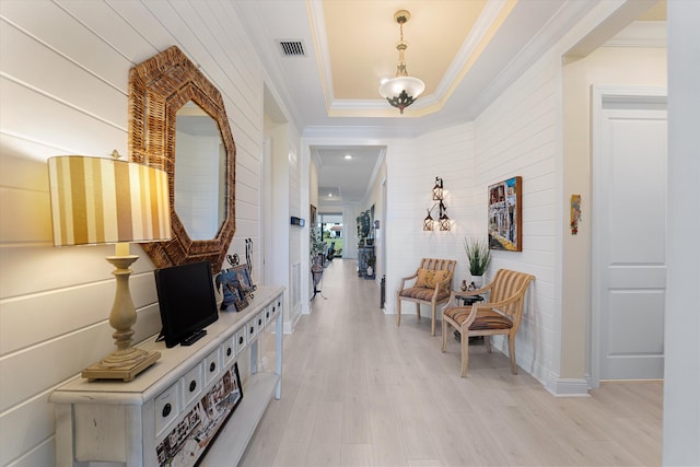 hallway with a chandelier, crown molding, a tray ceiling, and light hardwood / wood-style floors