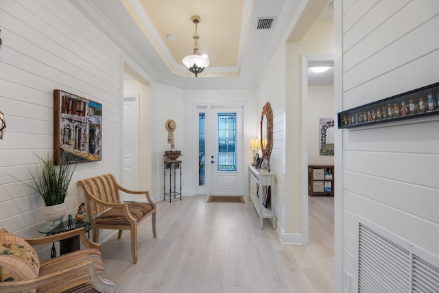 foyer with light hardwood / wood-style floors, a raised ceiling, and ornamental molding