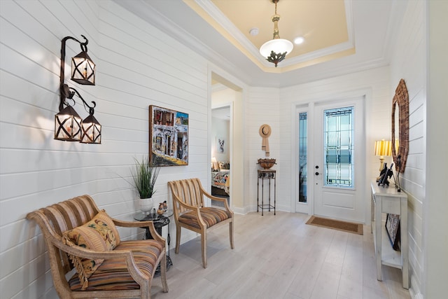 foyer featuring a raised ceiling, ornamental molding, and light wood-type flooring