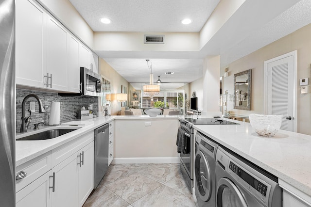 kitchen with sink, stainless steel appliances, light stone countertops, washing machine and dryer, and white cabinets