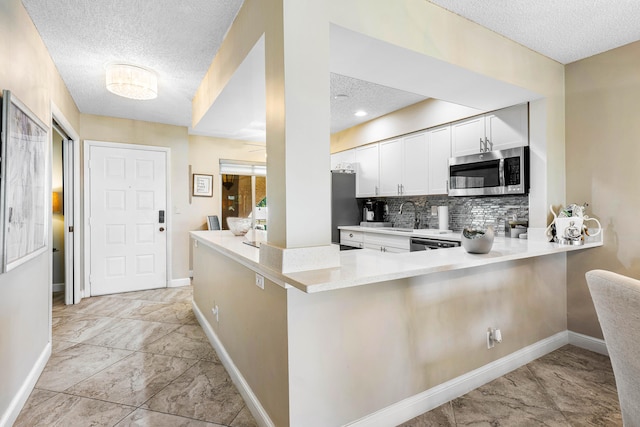 kitchen with stainless steel appliances, tasteful backsplash, white cabinets, kitchen peninsula, and a textured ceiling