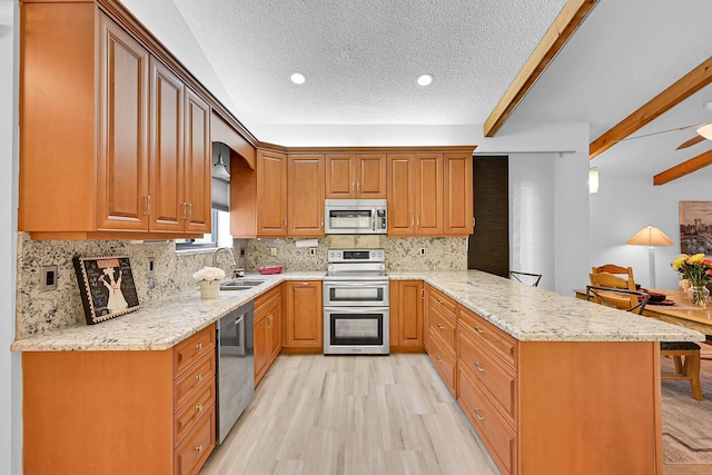 kitchen featuring appliances with stainless steel finishes, brown cabinetry, a sink, light wood-type flooring, and a peninsula